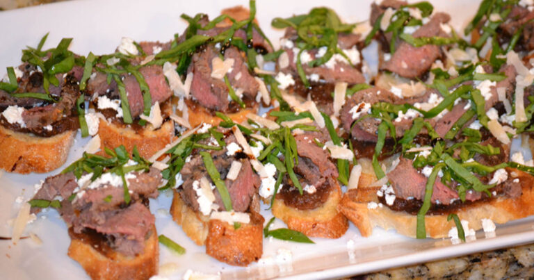 Sliced venison filet on top of baguette with toppings.