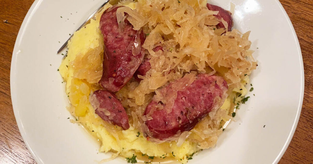 Venison kielbasa cooked with sauerkraut and apple served over homemade mashed potatoes