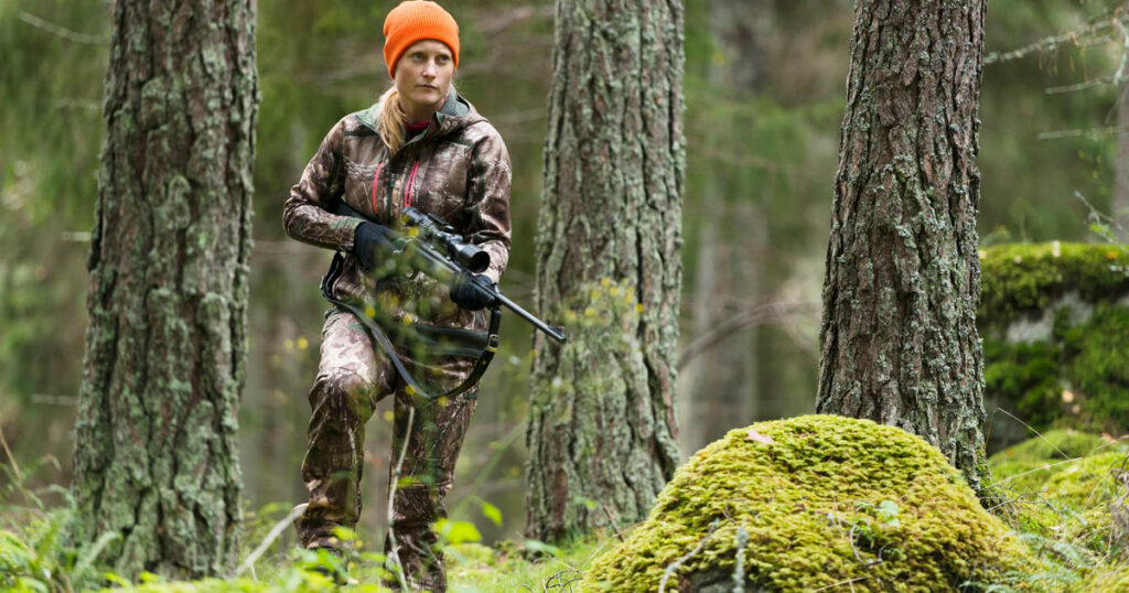 female hunter with rifle walking in woods